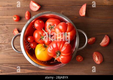 Différentes tomates dans la passoire sur fond de bois Banque D'Images