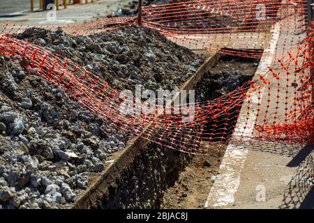 Travaux de réparation dans la rue de la ville. Une tranchée fraîchement creusée est clôturée avec un filet, pour la sécurité des citoyens Banque D'Images