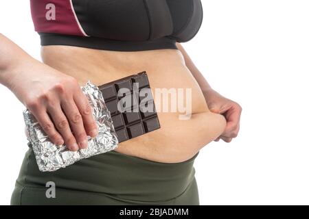 Femme avec excès de graisse sur son estomac avec du chocolat dans sa main. Image conceptuelle de l'obésité. Vue latérale, isolée sur un fond blanc. Banque D'Images