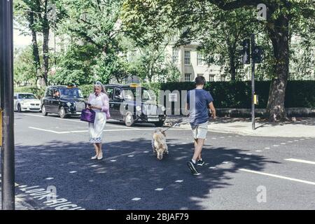 Londres/UK-30/7/18 : un jeune homme avec un chien et une femme traversant Grove End Road à St John's Wood sur un signal vert du feu de circulation alors que deux blac Banque D'Images