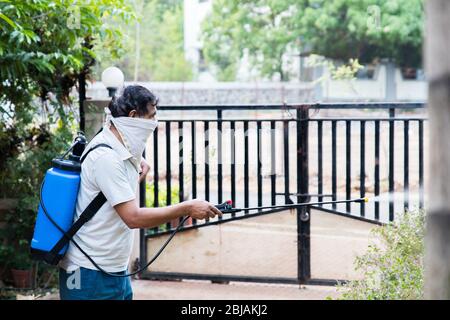 un mâle indien pulvérisant des pesticides dans son jardin à la maison en utilisant une pompe automatique avec un masque sur son visage Banque D'Images