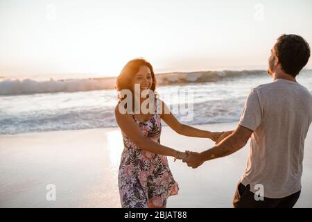 Rire jeune couple s'amuser à la plage au coucher du soleil Banque D'Images