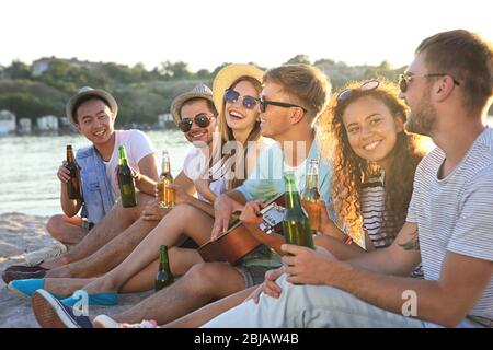 Groupe d'amis écoutant de la guitare et buvant de la bière à la plage Banque D'Images