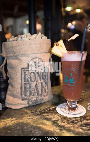 dh long Bar sac de salées arachides RAFFLES HOTEL SINGAPORE UN cocktail Singapore Sling en verre avec des noix de paille Banque D'Images