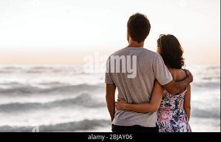 Un jeune couple affectueux qui regarde l'océan au coucher du soleil Banque D'Images