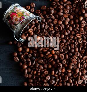 Grains frits de café frais parfumé, dispersés à partir d'un seau sur une table en bois Banque D'Images