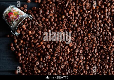 Grains frits de café frais parfumé, dispersés à partir d'un seau sur une table en bois Banque D'Images