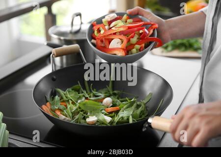 Mains mâles mettant des légumes dans la poêle se rapprochep Banque D'Images