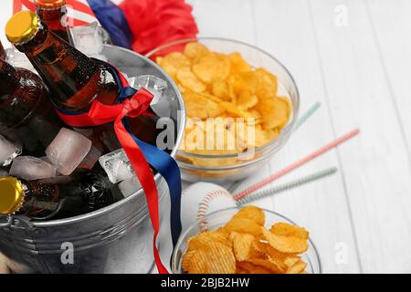 Seau avec bouteilles de bière, chips et boule sur fond blanc en bois Banque D'Images