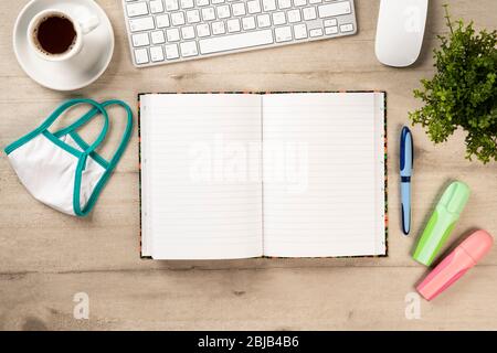 Bureau avec clavier, mobile, ordinateur portable, café et un masque de protection contre le virus corona et autres articles de papeterie sur fond de bois Banque D'Images