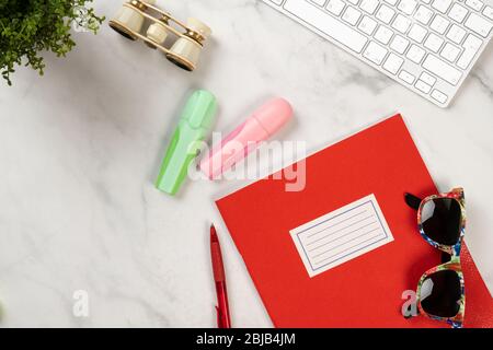 Photo d'un ordinateur portable, d'un clavier, de jumelles, d'un stylo, de marqueurs et de lunettes de soleil colorées sur un bureau en marbre blanc Banque D'Images