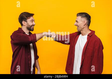 Deux jeunes amis heureux et heureux portant des vêtements décontractés isolés sur fond jaune, un geste de bosse de poing Banque D'Images