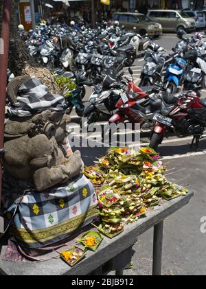 dh Balinese marché Carpark BALI INDONÉSIE ASIE statue de gardien hindou offre dans le parking trottinettes offre de la nourriture garée Banque D'Images