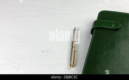 Élégant stylo et planificateur quotidien avec une housse en cuir vert sur un bureau en bois blanc Banque D'Images