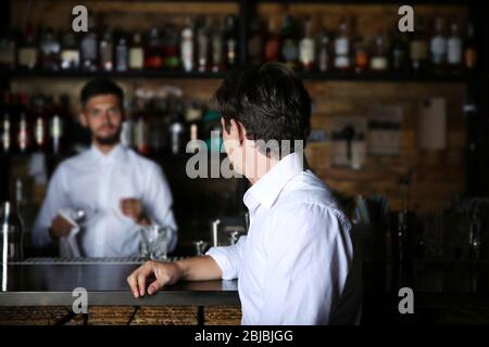 Homme en chemise blanche assis sur comptoir de bar en bois Banque D'Images