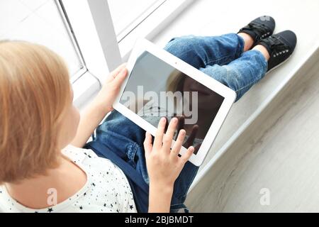 Jolie fille adolescente avec tablette assise près de la fenêtre Banque D'Images