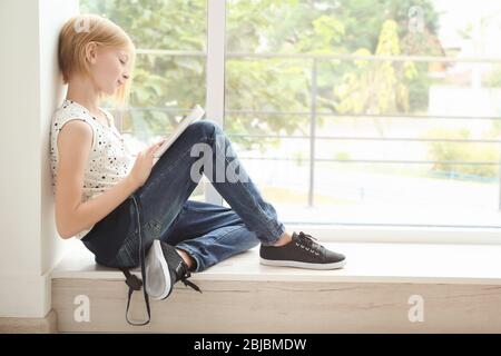 Jolie fille adolescente avec tablette assise près de la fenêtre Banque D'Images