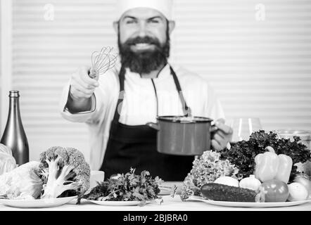 Utilisez un fouet manuel. Le chef professionnel tient le fouet et le pot. Fouetter comme pro. Homme barbu gars dans le tablier fouetter des œufs ou de la crème. Commencez à fouetter lentement la crème battante. Conseils et astuces pour fouetter la crème. Banque D'Images