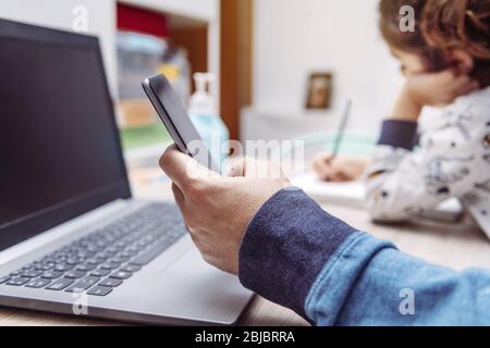 détail de la main d'un homme travaillant à la maison avec son ordinateur portable tenant un téléphone mobile alors que sa fille est en train de dessiner, travail à la maison concept en raison de la Banque D'Images