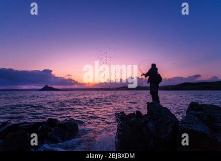 Un pêcheur jette dans la mer au coucher du soleil à Cornwall Banque D'Images