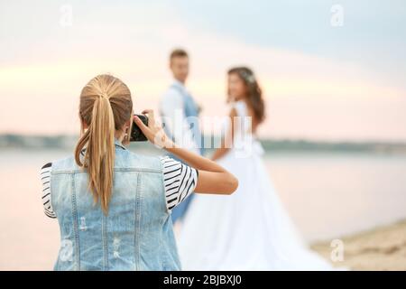 Jeune femme prenant photo de couple de mariage près de la rivière, vue rapprochée Banque D'Images