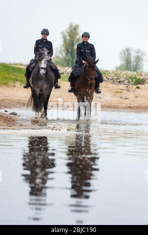 Bleckede, Allemagne. 29 avril 2020. Policewomen Yasmin Pröstler (l) et Anna Schloßer (r) font leurs chevaux de service le long des rives de l'Elbe lors d'une réunion de presse. Dans les semaines à venir, les officiers des escadrons équestres de Hanovre et Braunschweig doivent informer les visiteurs des règles de protection et punir les violations telles que le camping illégal et les feux ouverts. Crédit: Philipp Schulze/dpa/Alay Live News Banque D'Images