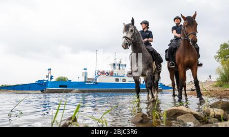 Bleckede, Allemagne. 29 avril 2020. Les policiers Yasmin Pröstler (l) et Anna Schloßer (r) sont debout avec leurs chevaux de service sur les rives de l'Elbe lors d'une réunion de presse, tandis que le ferry d'Elbe 'Amt Neuhaus' s'arrime en arrière-plan. Les responsables des escadrons équestres de Hanovre et Braunschweig doivent informer les visiteurs dans les prochaines semaines sur les règles de protection et punir les violations telles que le camping illégal et les incendies ouverts. Crédit: Philipp Schulze/dpa/Alay Live News Banque D'Images