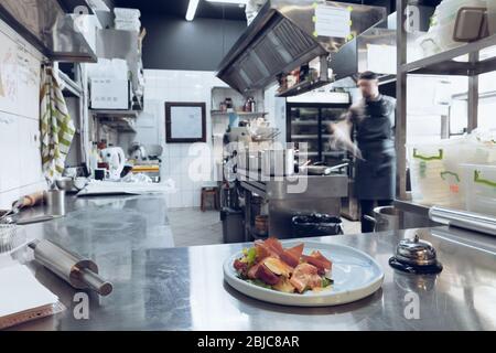 Dans les coulisses des marques. Le chef cuisine dans une cuisine professionnelle d'un repas de restaurant pour le client ou la livraison. Ouvrir des affaires de l'intérieur. Repas pendant la quarantaine. Se dépêchons-vous, mouvement. Banque D'Images