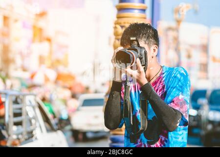 Un jeune photographe en vêtements mouillés utilise un appareil photo reflex numérique pour prendre des photos du festival d'éclaboussures d'eau Songkran sur la route dans la ville. Banque D'Images