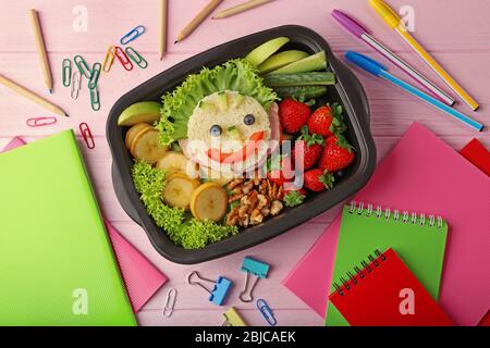 Lunchbox avec dîner et papeterie sur fond en bois rose Banque D'Images