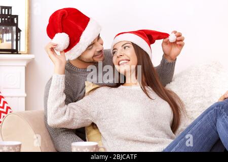 Jeune couple dans les chapeaux du Père Noël reposant à la maison Banque D'Images