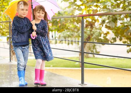 Mignons enfants sous un parapluie coloré dans le parc sous la pluie Banque D'Images