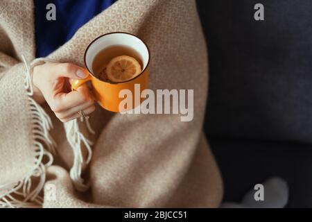Main de femme tenant une tasse de thé jaune avec citron par temps froid. Moments confortables, couverture en laine Banque D'Images