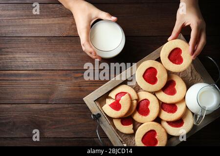 Mains féminines avec lait et biscuits sur table en bois, vue de dessus