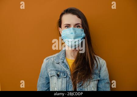 Photo de la femme brunette porte un masque médical de protection, en confiance dans l'appareil photo, porte une veste denim isolée sur fond brun. pa épidémique Banque D'Images