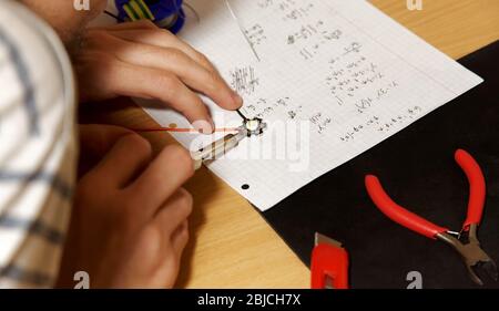 Jeune ingénieur étudiant en soudage simple filaire lambertian LED diode sur son bureau, mains closeup, tenant fer à souder. Espace de travail de fortune Banque D'Images