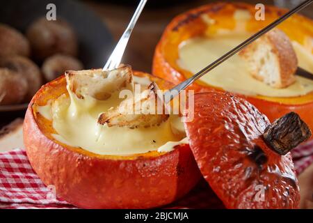 Fondue au fromage suisse traditionnelle dans une citrouille creuse pour un délicieux repas chaud d'automne en gros plan avec baguette grillée sur des fourchettes à tremper Banque D'Images