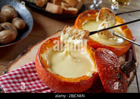 Service de fondue au fromage fondu dans un restaurant servi dans une citrouille rôtie, avec baguette grillée et pommes de terre pour la trempage et un verre de Banque D'Images