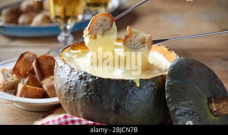 Service rustique de fondue au fromage dans une croûte de citrouille creuse rôtie avec baguette grillée pour plonger dans un gros vin blanc Banque D'Images