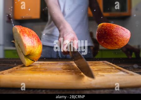 Chef coupe une pomme mûre jaune en deux avec un grand couteau en mouvement. Les éclaboussures d'eau et de jus volent dans différentes directions et gèlent dans l'air Banque D'Images