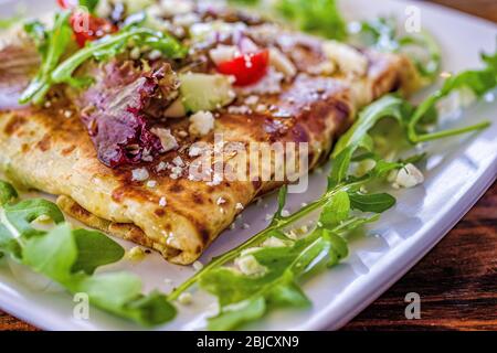 Face ouverte, crêpe sandwich avec arugula, feta fromage, concombre et tomates sur la plaque blanche. Banque D'Images