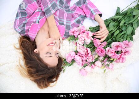 Jeune femme gaie avec beau bouquet de fleurs d'eustoma posé sur le lit à la maison Banque D'Images