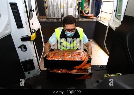 Un groupe de volontaires portant des masques de visage et des gants de protection emballe des fournitures de secours à distribuer dans un véhicule. Le Conseil communal de Penha de França a réalisé un projet appelé 'magasin d'alimentation sociale', lorsqu'une structure est utilisée pour stocker des produits alimentaires et d'hygiène personnelle donnés par les supermarchés et les écoles. Ces derniers sont emballés et ensuite distribués par des travailleurs bénévoles à des personnes, en particulier les personnes âgées et les malades, qui sont sans abri ou physiquement incapables, et qui sont dans une situation vulnérable en raison de la séquestration obligatoire en raison de la pandémie de COVID-19. Banque D'Images