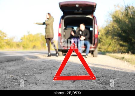 Triangle d'avertissement rouge sur route asphaltée. Couple prenant la voiture sur la route Banque D'Images