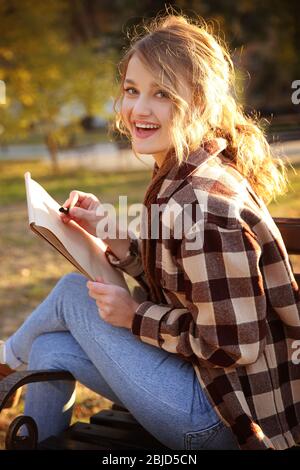 Jeune artiste féminine dessinant un croquis tout en étant assise sur un banc dans un beau parc Banque D'Images