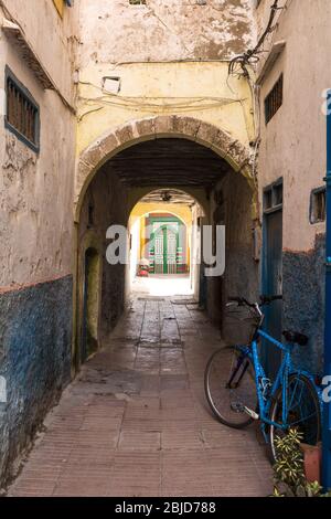 Rue étroite avec un vélo et une plante dans un pot. Passe-bas avec un arc et une porte éclairée colorée en arrière-plan. Vieille ville (médina) d'Essaouira, Banque D'Images