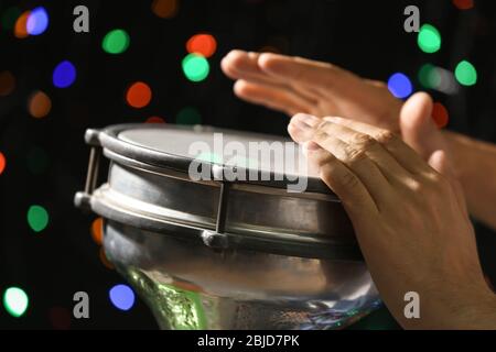 Les mains de l'homme jouant le tambour africain contre les lumières défocused, gros plan Banque D'Images