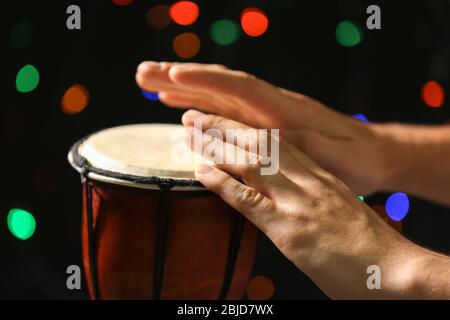 Les mains de l'homme jouant le tambour africain contre les lumières défocused, gros plan Banque D'Images