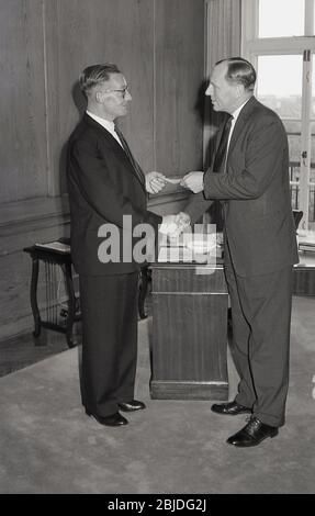 Années 60, historique, dans un élégant bureau lambrissé, une entreprise directeur général présentant un chèque à un employé de longue date, Angleterre, Royaume-Uni. Banque D'Images