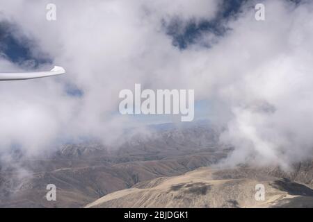 aérien, d'un planeur, avec pointe d'aile parmi les nuages blancs qui se cachent au-dessus des pentes stériles, tourné en lumière vive au-dessus de st. Plage de Bathan, Canterbury, île du Sud Banque D'Images